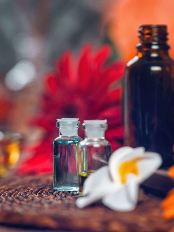 Aromatherapy composition with transparent aromatherapy bottles filled with blue and green essential oils, colorful red and orange flowers and candles. Aromatherapy relax concept.