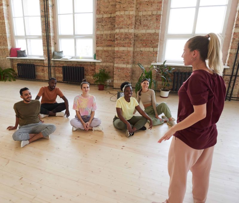 Rear view of young instructor talking to her team before sports training in dance studio
