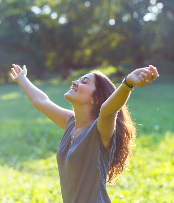Portrait of beautiful brunette woman in park with her arms outstretched.