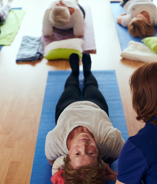 Top view of group of senior women engage in various yoga exercises, including neck, back, and leg stretches, under the guidance of a trainer in a sunlit space, promoting well-being and harmony.