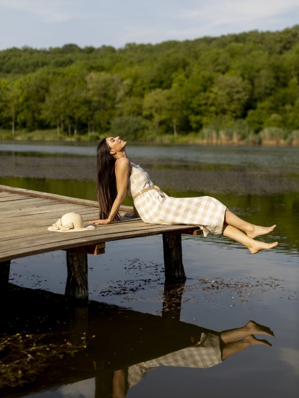 Young woman relaxing on the wooden pier at the calm lake on a hot summer day